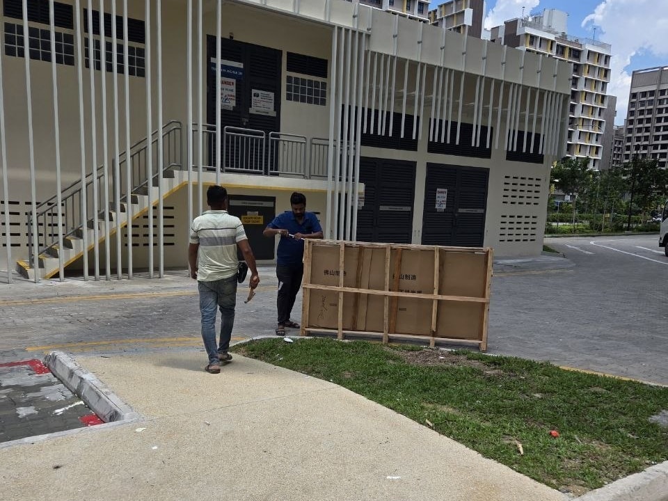 Two movers with a wooden crate stamped 佛山制造 (made in Foshan) at the foot of a new HDB block