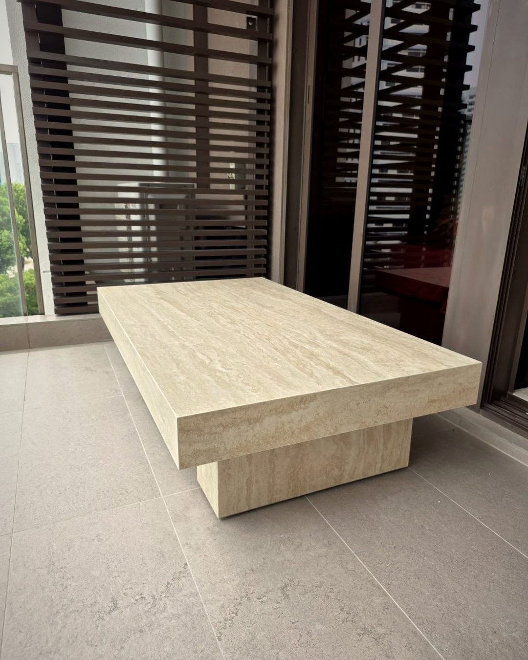 A bare new flat with large pale floor tiles, full-height windows and a single travertine table