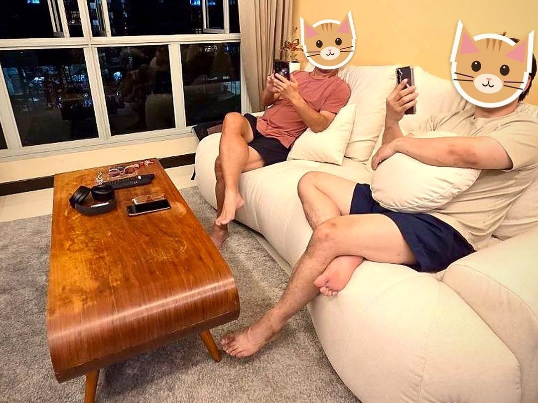 Two people relaxing on a cream sofa beside a timber coffee table in an HDB living room at night