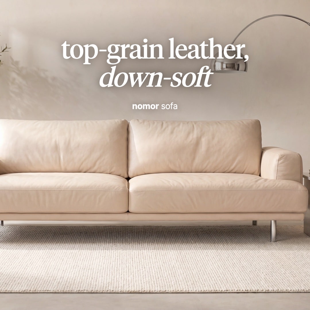 Nomor sofa in cream leather on slim metal legs beside an arc floor lamp. The image reads "top-grain leather, down-soft, nomor sofa".