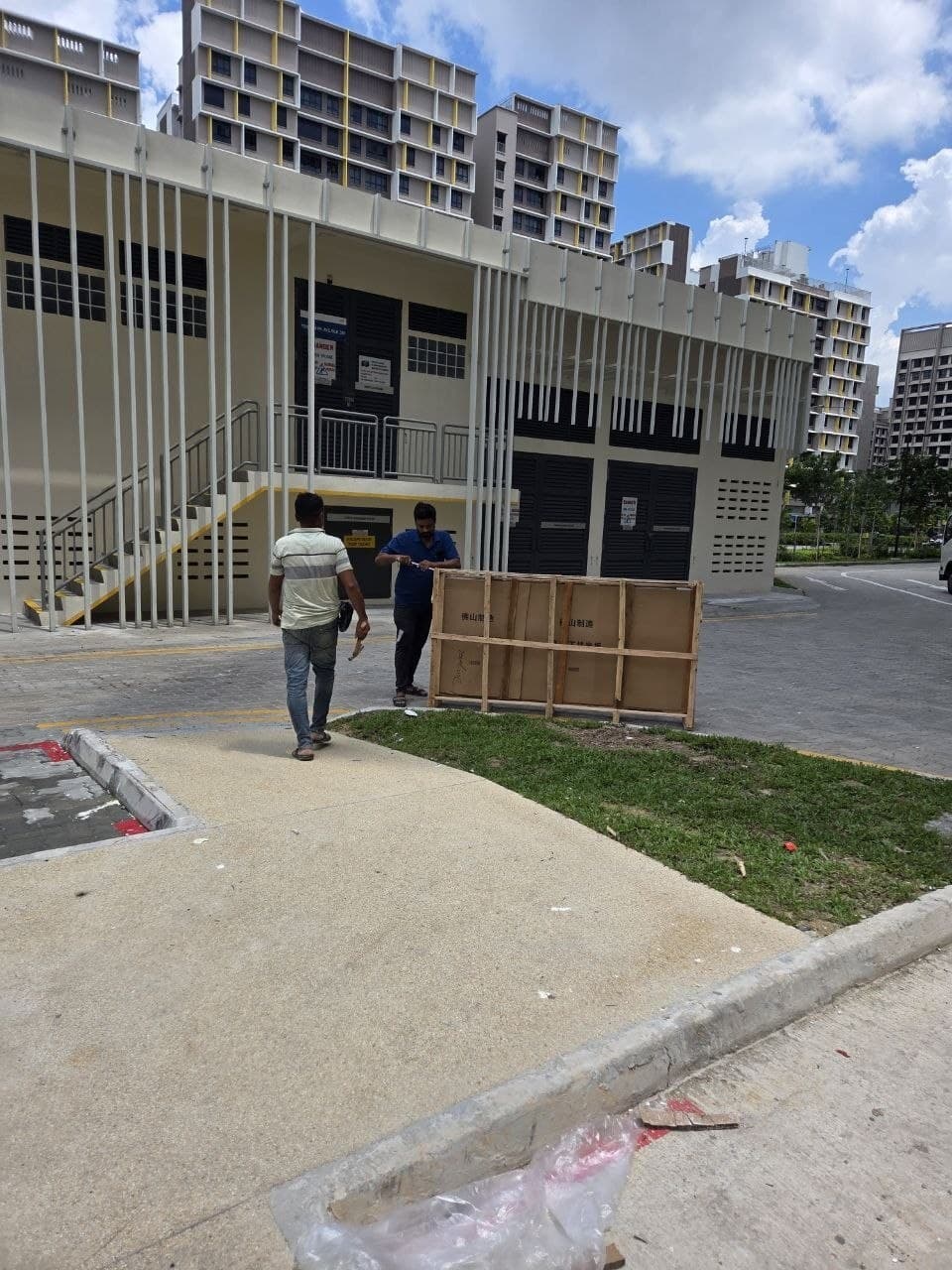 Two movers with a wooden crate stamped 佛山制造 (made in Foshan) at the foot of a new HDB block