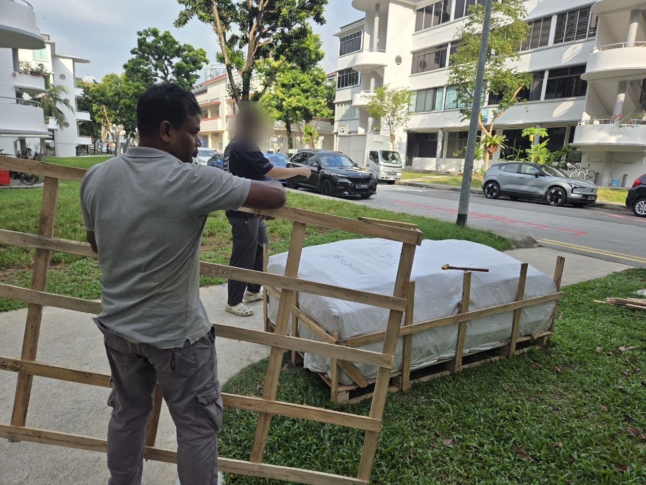 Movers unpacking a crated sofa on the grass outside an HDB block in Tiong Bahru