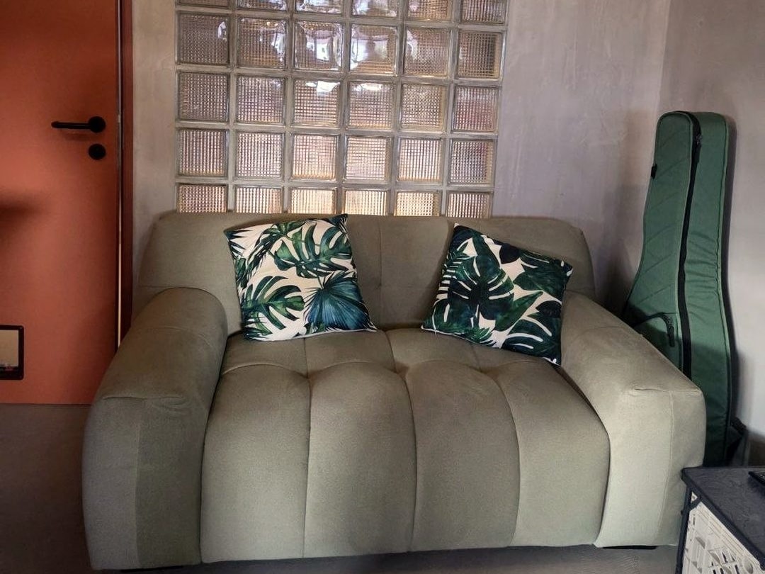 A sage-green custom Vella sofa with leaf-print cushions under a glass-block wall
