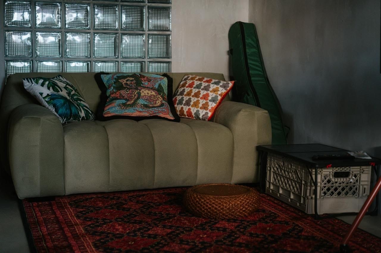 A sage-green Vella sofa against a glass-block wall, styled with patterned cushions on a red rug