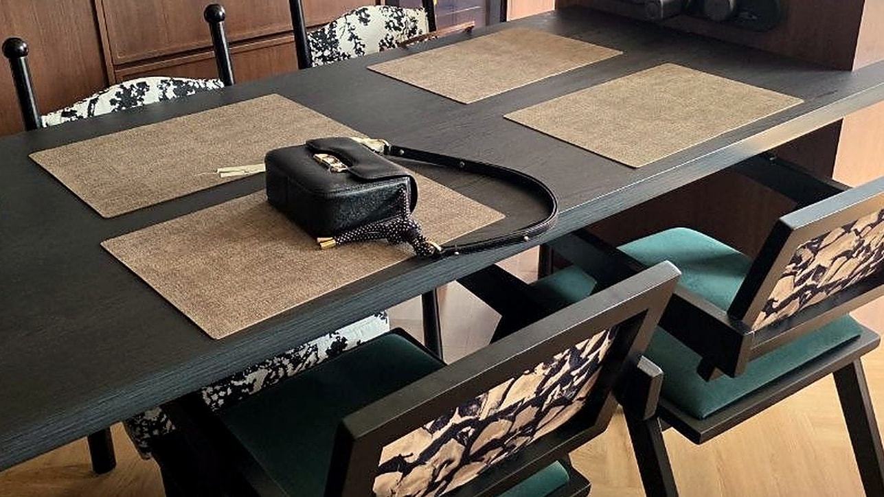 A dark timber dining table set with woven placemats, with patterned dining chairs and teal seats