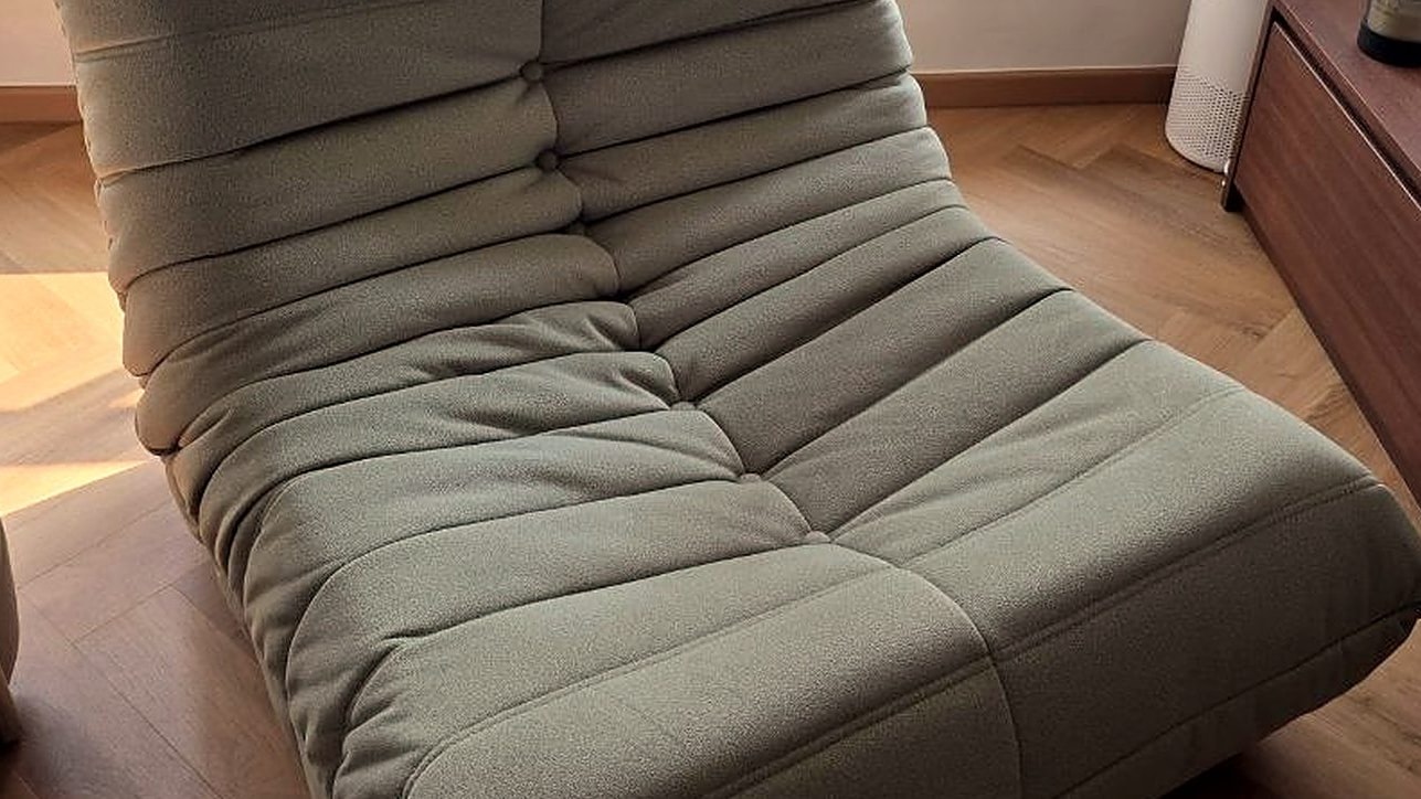 A moss-green Rosae lounge chair on a herringbone timber floor beside a walnut console