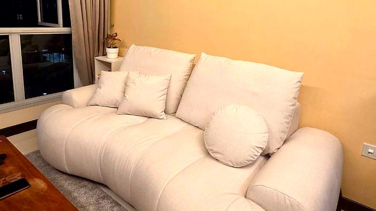 A cream Voado sofa with round bolster cushions against a warm orange wall at night