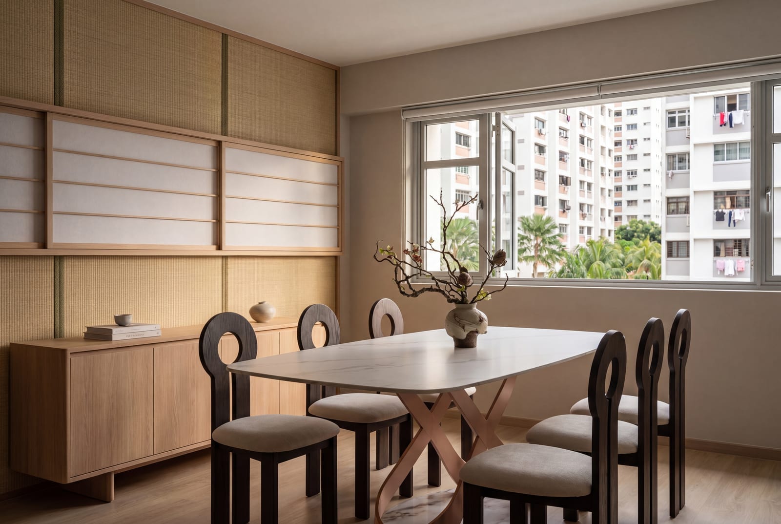 A white stone-topped dining table with soft grey veining on a sculpted pale base, with dark wood chairs, in a Japandi-style HDB dining room