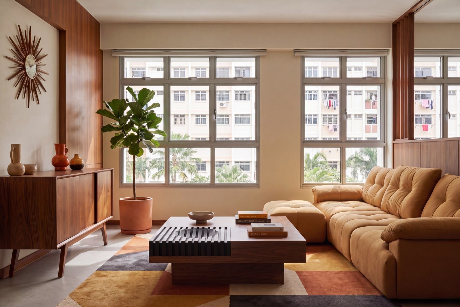 A tan tufted sofa with an extended chaise seat and ottoman beside tall windows in an HDB living room